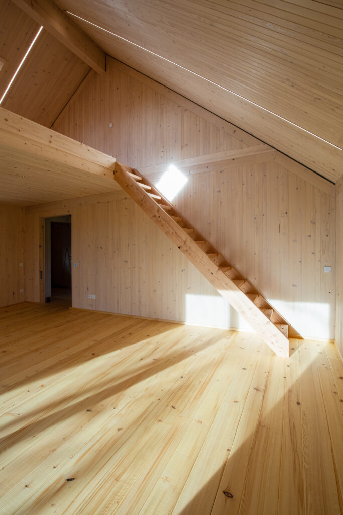 Raum in Holzbauweise mit Sonnenlicht und Treppe zur Galerie