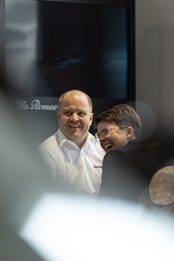 Verkäufer mit Junior-Chefin beim Gespräch lachend im Autohaus Deschberger